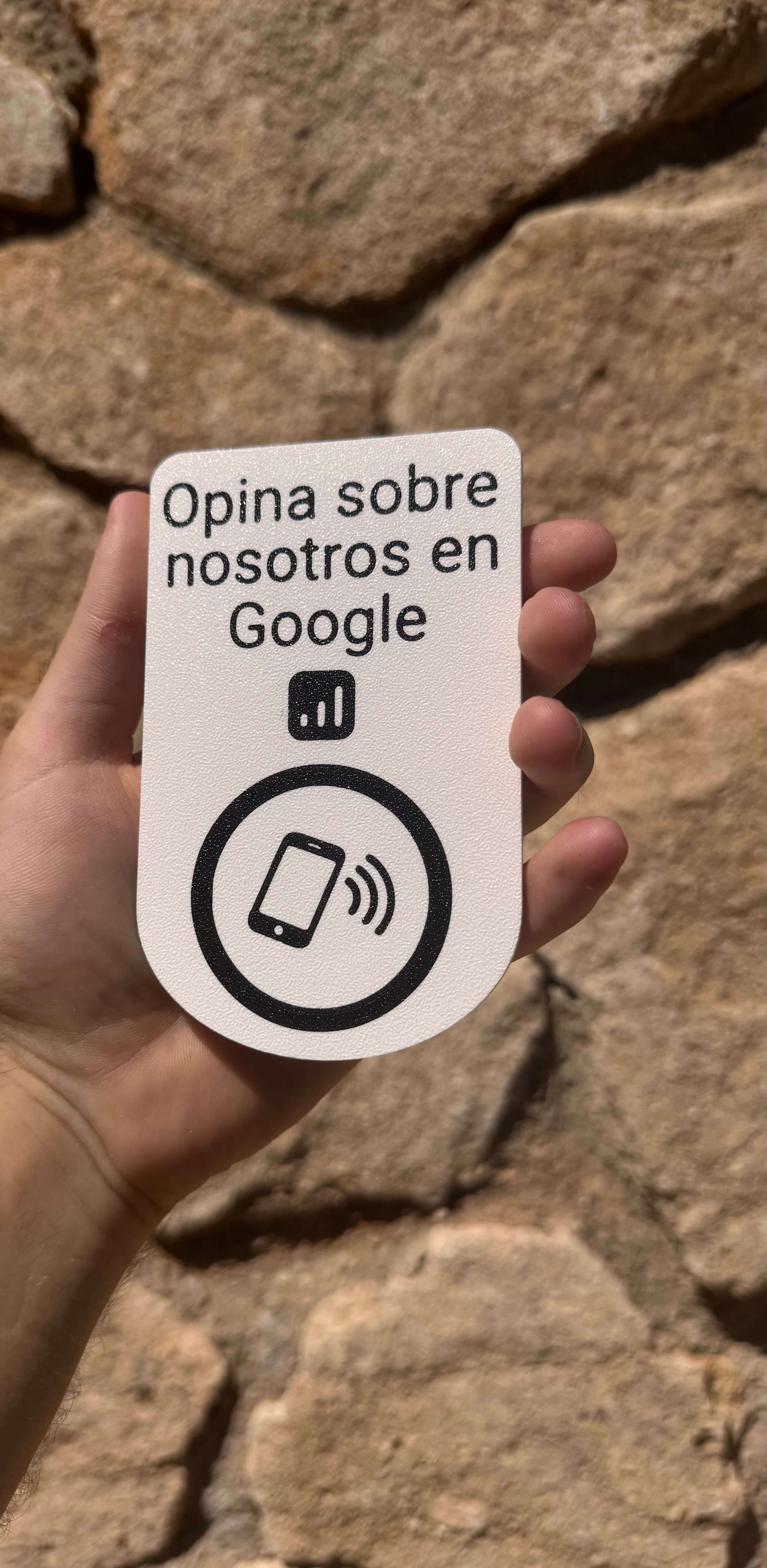 Placa NFC para dejar reseñas en Google sujetada con la mano junto a un muro de piedra