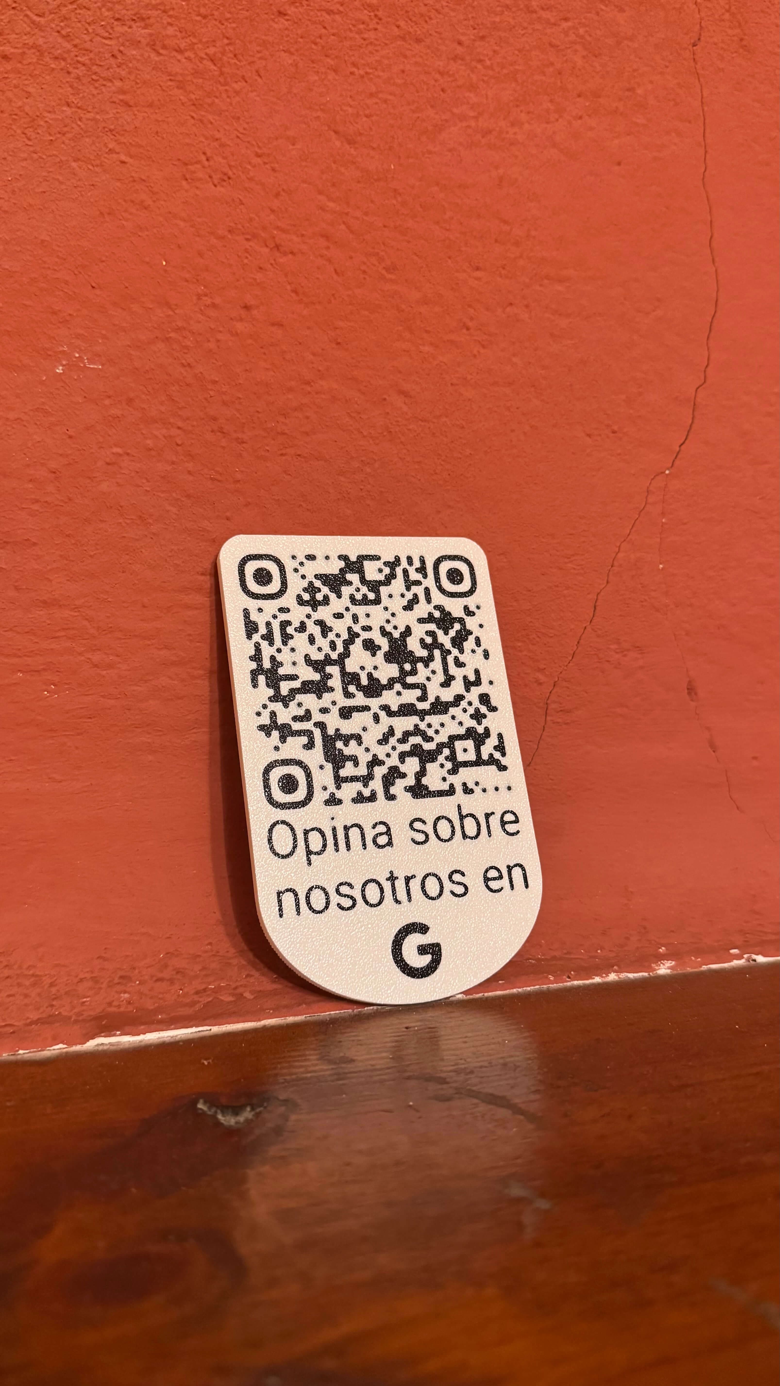 Placa QR de reseñas de Google apoyada sobre una repisa de madera junto a una pared roja