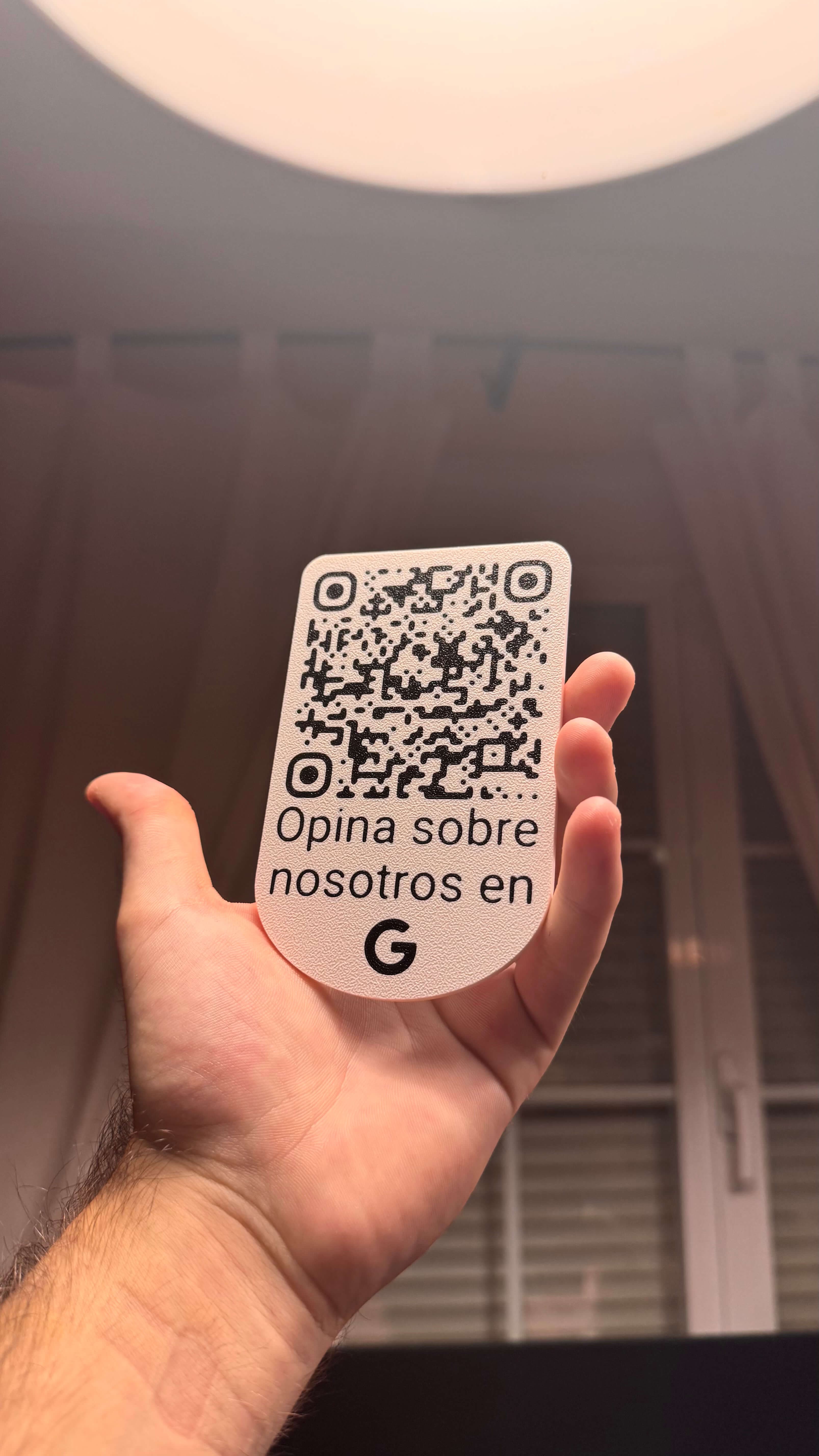 Placa QR de reseñas de Google sujetada con la mano bajo una luz de techo